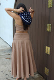 Woman in a beige dress standing in front of a wooden door with gold hinges.