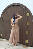 Woman in a beige dress with a blue scarf standing in front of a wooden door.